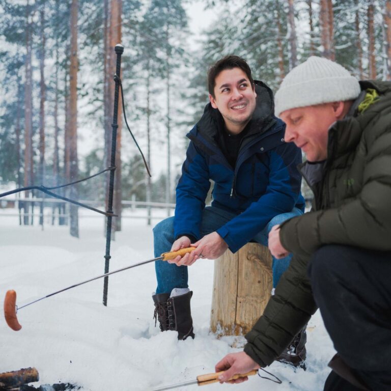 Men grilling sausages at wintery campfire.