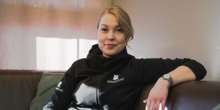 Nainen istuu rennosti sohvalla ja hymyilee kameraan.