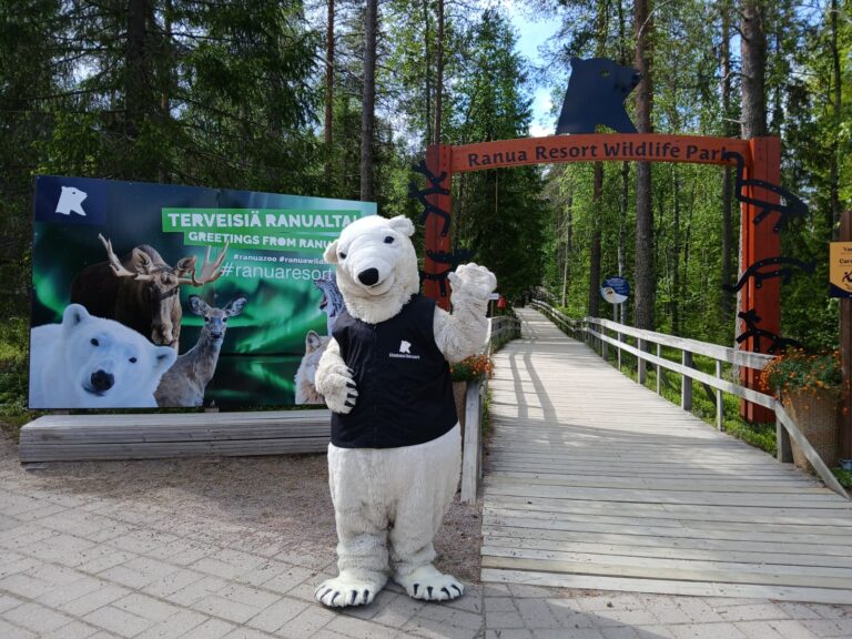 Jonne Jääkarhu maskotti vilkuttaa kameraan eläinpuiston portilla.